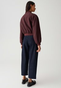 Giacca pullover borgogna con vita elastica arricciata, abbinata a pantaloni a gamba larga blu scuro e scarpe nere. Tessuto liscio e strutturato.