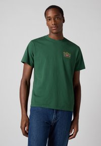 Groene katoenen T-shirt met een ronde hals en korte mouwen. Bevat kleine, veelkleurige grafische details op de borst.