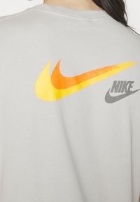 Person wearing a light gray shirt with a large yellow-orange Nike swoosh and smaller gray Nike logo on the upper back.