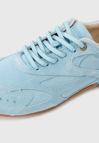 Baskets en daim bleu clair avec lacets plats, coutures détaillées et semelle en caoutchouc marron sur un fond clair.