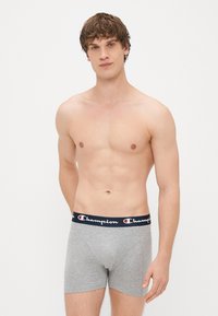Boxer-briefs en coton gris avec une taille en bleu marine portant le logo "Champion" en rouge et blanc. Texture lisse, design ajusté.