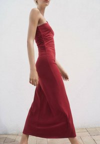 Rochie maxi roșie, cu dungi, cu un corset ajustat, decolteu drept și o fustă fluidă, prezentată pe un fundal alb.