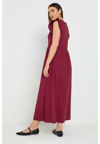 Burgundin pitkä mekko, jossa on puffihihat ja tiukka yläosa, joka on kerätty vyötärölle. Yhdistetty mustiin tasapohjaisiin kenkiin, joissa on pyöreä korostus.