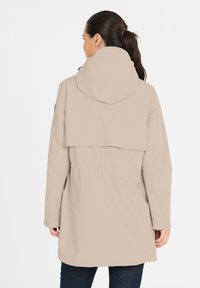 Jacket imperméable beige avec capuche, taille élastique et rabat au dos. Comprend des manches longues et une coupe droite, fabriqué en matériau lisse et léger.