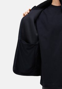 Schwarze Jacke mit Reißverschluss und leichtem Innenfutter, ausgestattet mit einer großen Innentasche und einem weichen, strukturierten Kragen.
