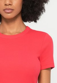 Κόκκινη ριγωτή μπλούζα με κοντά μανίκια και στρογγυλή λαιμόκοψη. Το ύφασμα είναι λείο με ελαφριά ελαστικότητα, τονίζοντας μια εφαρμοστή σιλουέτα.