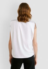 Valge ilma varrukateta pluus, millel on narmastega õlavarre aktsendid ja pehme kangas, rõõmsat lõikega ja külgjaotustega, mis tagavad liikumise mugavuse.