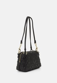 Svart vadderad handväska med rundad form, guldfärgad metall, dubbla remmar och en präglad logotyp framtill. Dragkedja på ena sidan.