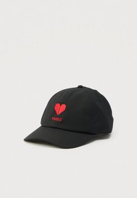 Black baseball cap with red origami-style heart and "HUGO" embroidered on front, set against a plain white background.