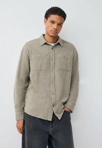 Light grey herringbone flannel shirt with two front pockets and button closures. Features a collar and long sleeves. Paired with dark jeans.
