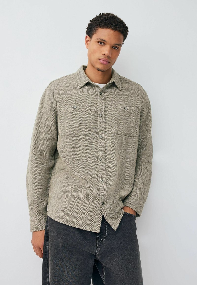 Light grey herringbone flannel shirt with two front pockets and button closures. Features a collar and long sleeves. Paired with dark jeans.