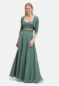 Zielona, długa sukienka z dopasowanym koronkowym gorsetem i zwiewnym dołem. Akcentowana rękawami o długości trzech czwartych, o jedwabistej fakturze i połysku.