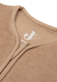 Haut en coton beige avec une texture en éponge, tissu doux et col rond. L'étiquette à l'intérieur indique la marque et les instructions d'entretien.