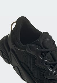 Černá sportovní bota s texturovaným svrškem, polstrovaným límcem a zesílenými dírami na tkaničky. Disponuje výrazným logem a odvážnou, tvarovanou podešví.