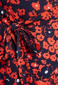 Kukkakuvioinen kietaisumekko, jossa on tummansininen tausta, punaisia ja valkoisia kukkakuoseja sekä sidottava kangashihna. Sujuvaa, kevyttä materiaalia.