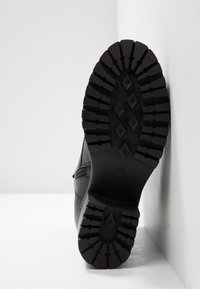 Czarny but z teksturowaną gumową podeszwą z głębokim bieżnikiem i zamkiem bocznym, wykonany z gładkiej skóry z wzmocnionymi przeszyciami.