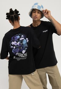 Zwei Personen tragen schwarze "Memorize"-T-Shirts; eine zeigt ein Rückendesign mit Koi-Fischen und Blumen, die andere schaut nach vorne und trägt einen blaukarierten Fischerhut.