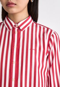 Rød og hvid stribet skjorte med button-down krave, udstyret med et lille broderet logo og knaplukning. Lavet af et letvægtsstof.