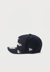 Casquette bleu marine avec une visière incurvée, comportant un texte brodé blanc à l'avant et un logo sur le côté. Fabriquée en tissu texturé.