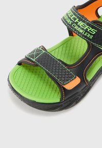 Czarno-zielone sandały z teksturowaną cholewką, pomarańczowymi akcentami, regulowanymi paskami i wyściełaną zieloną wkładką. Lekka konstrukcja.