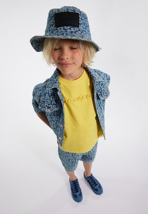 Set di giacca in denim e pantaloni corti con stampa del logo blu, abbinato a una maglietta gialla e scarpe da ginnastica blu. Include un cappello a secchiello con una patch del logo.