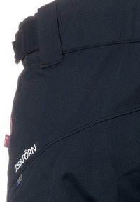 Mörkblå skidbyxor med en texturerad yta, med en logo, bältesöglor och förstärkt söm. Inga fickor synliga i närbilden.