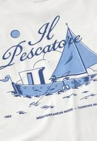 Voilier avec pêcheur lançant une ligne sur l'eau sous le texte "Il Pescatore" et "Mediterranean Mode – Thinking Mu" daté de 1983 sur tissu blanc.