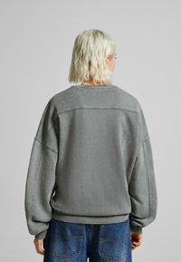 Sweat-shirt gris oversize avec encolure ronde, épaules tombantes et poignets côtelés, présentant une texture lisse et un design minimaliste.