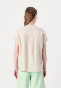 Top in lino a righe beige chiaro con maniche corte, scollatura tonda e una piega centrale sul retro, abbinato a pantaloni corti verde menta.