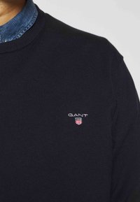 Granatowy sweter z dzianiny z okrągłym dekoltem, z małym haftowanym logo na klatce piersiowej i teksturowanym wykończeniem materiału.