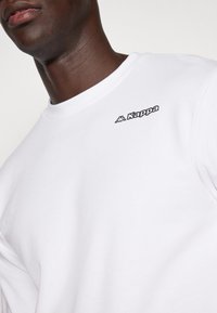 Sweatshirt blanc avec un col rond et le logo Kappa en noir sur la poitrine. Fabriqué en tissu doux avec une texture lisse.