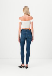 Jeans din denim albastru subțire, cu buzunare la spate, asortați cu un top alb off-the-shoulder. Croiala impresionantă pune în evidență formele. Pantofi negri cu toc.