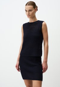 Top sans manches en tricot bleu marine avec un motif texturé à tissage ouvert, associé à une jupe ajustée assortie, offrant un look contemporain.