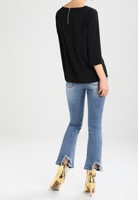 Svart, löst sittande topp med trekvartslånga ärmar och en silverdragkedja i ryggen, tillsammans med ljusblå utsvängda jeans och guldklackade stövlar.