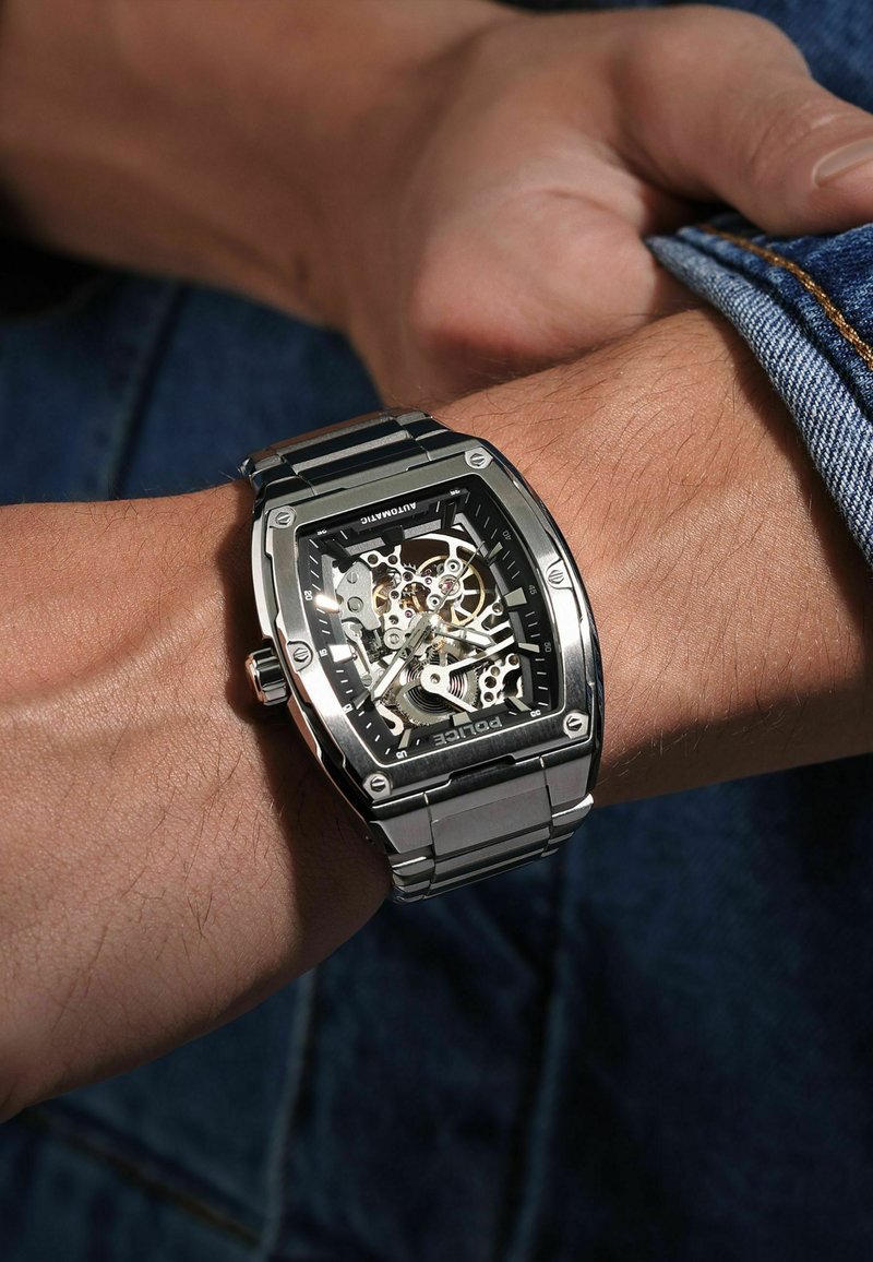 Zegarek automatyczny o szkieletowym designie, czarna tarcza, srebrna stal nierdzewna, prostokątna koperta oraz widoczne mechanizmy i tryby.