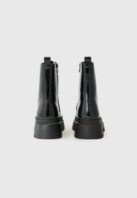 Bottines noires avec une finition brillante, semelles en caoutchouc épaisses, zips sur les côtés et languettes à l'arrière pour un enfilage et un retrait faciles.