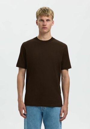 Braunes Baumwoll-T-Shirt mit Rundhalsausschnitt und kurzen Ärmeln, kombiniert mit hellblauen Jeans. Schlichtes Design, keine sichtbaren Muster oder Akzente.