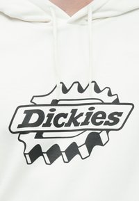 Λευκό hoodie με μαύρο λογότυπο Dickies και σχήμα φόντου με αιχμηρέ ς άκρες. Μαλακό ύφασμα, κορδόνια στη κουκούλα και άνετη εφαρμογή.
