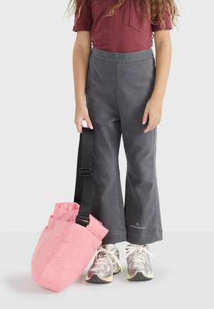 Rosa, gepolsterte Tasche mit Schulterriemen und grauen, weiten Hosen, kombiniert mit silbernen Sneakern. Das Hemd ist kastanienbraun mit einer Brusttasche.