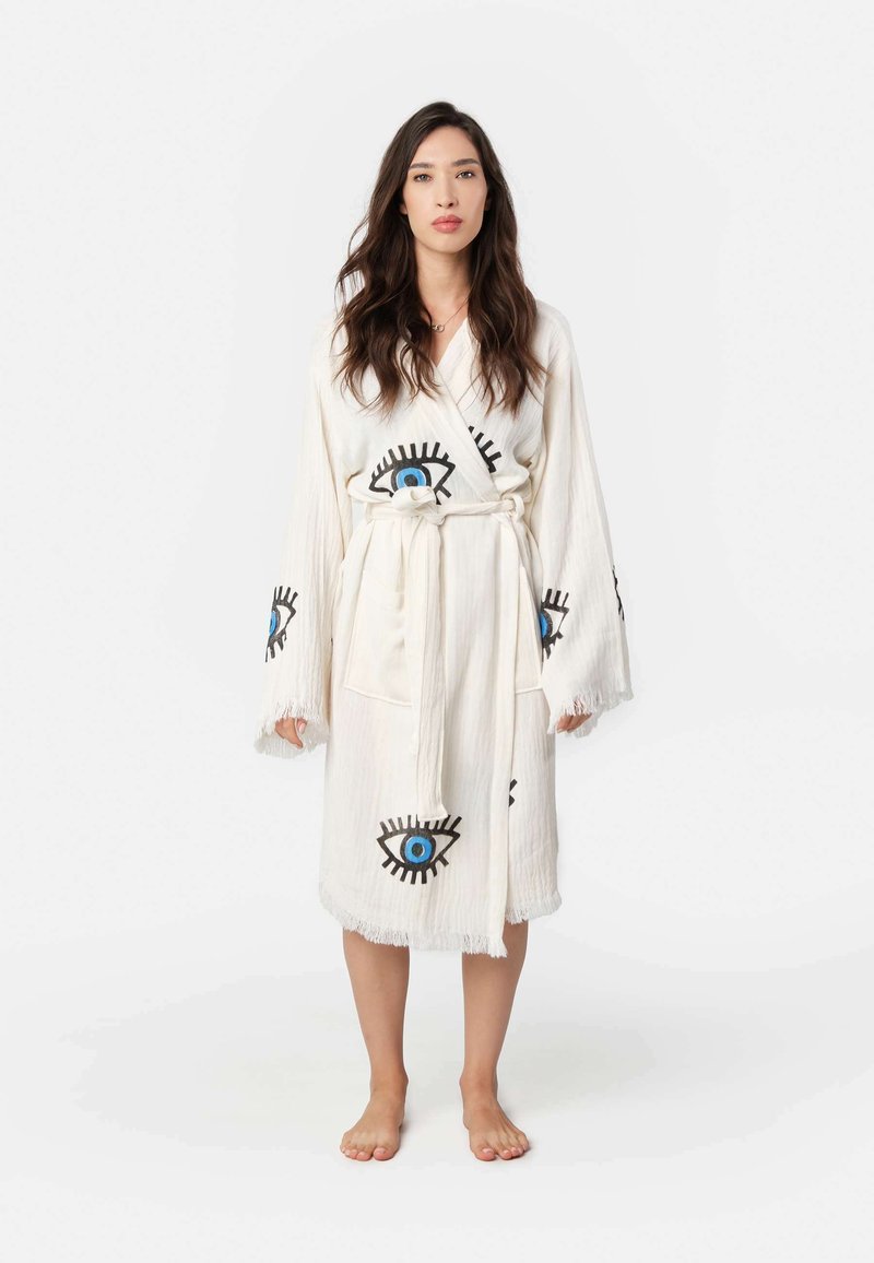 Biely róba s čierno-modrými grafickými očami, s strapcovými rukávmi a viazacími pásikmi. Vyrobená z ľahkého materiálu, má prednú vrecko.