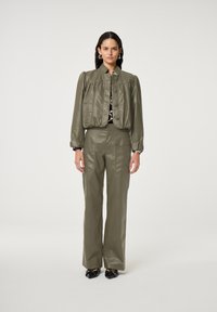 Olijfgroene nepleer cropped jack met opgeblazen mouwen, gecombineerd met bijpassende hoge taille broek met zijzakken. Zwarte schoenen.