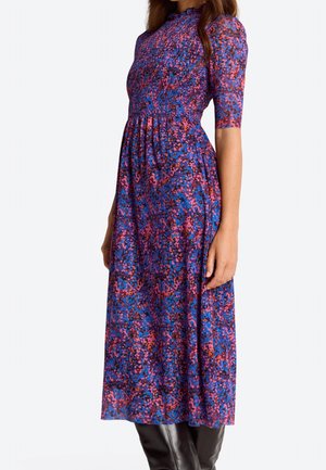 Długa fioletowa sukienka z kwiatowym wzorem w kolorach niebieskim, różowym i pomarańczowym. Posiada marszczony karczek i krótkie rękawy. Noszona z czarnymi kozakami sięgającymi do kolan.