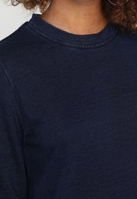Marineblaue Sweatshirt mit rundem Ausschnitt und sichtbaren Nähten. Der Stoff wirkt weich und strukturiert und unterstreicht das legere Design.