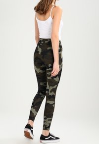 Kamouflageleggings i gröna, svarta och beiga nyanser, med hög midja och en åtsittande silhuett. Matchad med svarta sneakers.