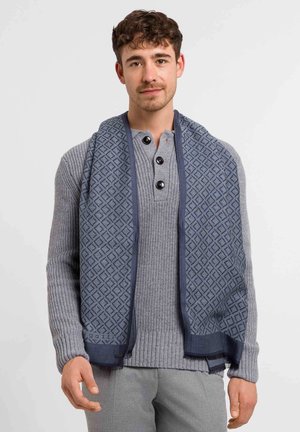 Navy patterned scarf with a geometric design, layered over a light gray ribbed sweater with a henley collar and dark buttons.