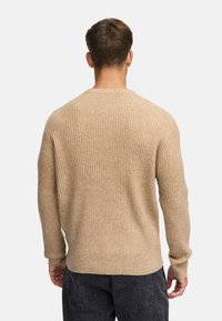 Maglione beige a coste con maniche lunghe, collo rotondo e texture sottile. Il retro presenta un orlo leggermente più lungo.