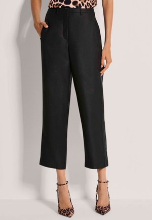 Schwarze, kurze Hosen mit glatter Textur, Seitentaschen und flacher Vorderseite. Kombiniert mit Leopardenmuster-Pumps und einem passenden Oberteil.