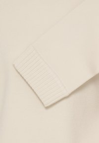 Gros plan sur la manche d'un pull de couleur crème avec un bord-côte, montrant une texture douce et lisse de tissu tricoté.