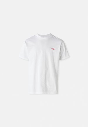 T-shirt en coton blanc avec un col rond et des manches courtes, orné d'un petit logo rouge "OBEY" sur le côté gauche de la poitrine.
