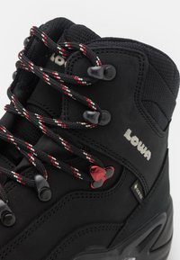 Czarne buty trekkingowe z teksturowanym materiałem, sznurowadłami z czerwonym akcentem i etykietą wodoodporną Gore-Tex. Posiadają metalowe oczka i wyściełany kołnierz.
